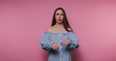 Komik bir yüz ifadesi takınarak, pembe arka planda duyguların etkileşimini gösteren, mizahi bir şekilde hüzün taklidi yapan genç bir kadının görüntüleri.