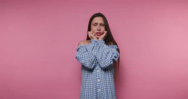 Genç bir kadının görüntüsü şaşkın ve düşünceli görünüyor. Pembe arka plandayken yüzüne dokunuyor.