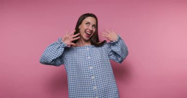 Genç bir kadının görüntüsü düşünceli bir yüz ifadesi sergilerken pembe arka planda büyüleyici bir pozla yanaklarını işaret ediyor.