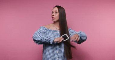 Moda dünyasından genç bir kadının görüntüsü, saç fırçasıyla özgüvenli bir şekilde poz veriyor. Bu görüntüler, evcilliğinin ve duruşunun ilgi çekici bir karışımını gözler önüne seriyor..