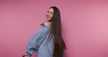 Genç, neşeli bir kadının, neşeli bir şekilde saçlarını savurup pembe arka planda neşeli bir anı yakaladığı görüntüler.