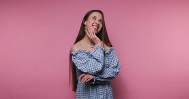 Düşünceli genç bir kadının görüntüsü yan tarafa bakıyor. Yüzü pembe arka planda derin düşüncelere dalmayı yansıtıyor.