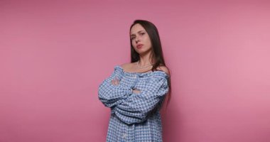 Genç bir kadının görüntüsü kollarını kavuşturup pembe arka planda moda anlayışını ve kendine güvenini gösteriyor.