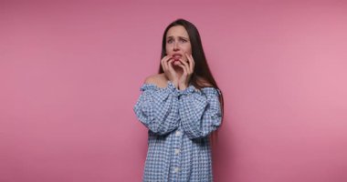 Genç bir kadının tırnaklarını endişeyle yerken çekilmiş görüntüleri, pembe arka planda endişe ve endişeyi yansıtıyor.