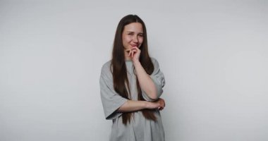 Genç bir kadının görüntüsü, çenesinde bir parmak ile neşeli bir poz verir. Derin düşüncelere işaret ederken, ışık arka planında cazibe yayar.