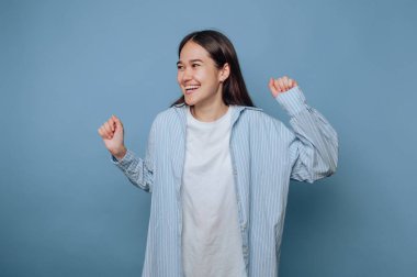 Genç bir kadın, yüzünde kocaman bir gülümsemeyle neşeli bir şekilde dans etmekten zevk alır. Çizgili bir gömlek ve sade bir tişört giyer, kaygısız ruhunu ön plana çıkarır..