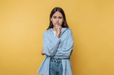 Kolları çapraz duran bir kız açık mavi çizgili bir gömlek giyiyor. Dalgın bir bakışı var. Dalgın dalgın dalgın dalgın dalgın, arkasında parlak sarı bir duvar var..