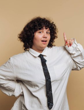 Kıvırcık saçlı biri bol beyaz gömlek giyer ve siyah kravat takar. Kendine güvenen bir ifadeyle şakacı bir şekilde yukarı bakar. Arka plan yumuşak, nötr bir renktir..