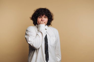 Bir insan, tedirgin bir şekilde tırnaklarını yiyen basit bir bronzlaşma arkaplanının karşısında durur. Beyaz gömlek ve siyah kravat takarlar. İfadelerinde endişe ve endişe taşırlar..