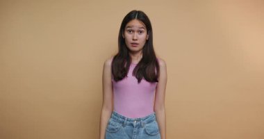 Genç bir kadın, basit bir sarı arkaplan önünde dururken şaşkınlık ve şaşkınlık içeren bir dizi duygu sergiliyor. İfadeleri her karede değişiyor, büyüleyici izleyiciler..