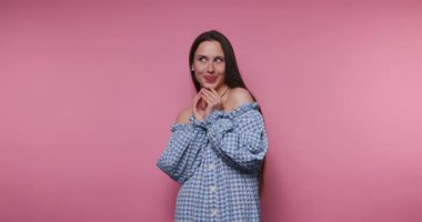 Mavi omuzsuz elbiseli bir kadın pembe bir duvarın önünde mutluluk ve neşe ifade eder. Gülümserken ve kişiliğini gösterirken farklı pozlar veriyor..