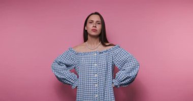 Mavi kareli bluz giyen bir kadın pembe bir arka plana karşı bir dizi duygu sergiliyor. Düşüncelerini açıkça ifade etmek için el hareketlerini ve yüz ifadelerini kullanıyor..
