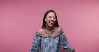 Genç bir kadın neşe dolu ruhunu gülücükler ve kahkahalarla paylaşıyor. O enerjik kişiliğini sergilerken onun renkli kıyafeti canlı pembe arka plana karşı çıkıyor..