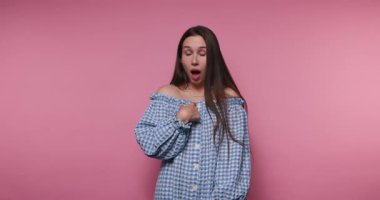 Bir kadın, neşeli bir şekilde poz verirken şaşkınlıktan şaşkınlığa kadar çeşitli duygular gösterir. Neşeli seans canlı pembe bir duvarın önünde geçiyor..