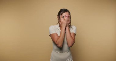 Bir kadın ellerini şakaya vurarak yüzünü kapatır ve farklı duygular gösterir. Sade bir arka plana karşı poz veriyor, neşeli bir hava yaratıyor. Her kare onun neşeli ruhunu yakalıyor..