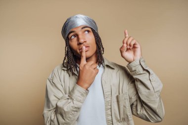 Tarafsız bir ortamda, örgülü saçı olan genç bir insan derin düşüncelere dalmış, yeni bir fikre işaret eder gibi parmağını kaldırıyor. Düşünceli ifadeleri yaratıcılık ve ilham veriyor..