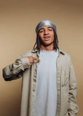 Genç bir adam rahat bir tavırla duruyor, gömleğini gösterirken hafifçe gülümsüyor. Gümüş başörtüsü hafif kıyafetini tamamlıyor, şık bir görünüm yaratıyor..