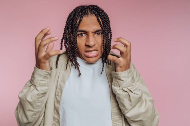 Genç bir adam ellerini pembe bir arka planda saçlarıyla gezdirirken yoğun bir ifadeyle hayal kırıklığı yaşıyor. Ayarlar onun saf duygularını ve enerjisini vurguluyor..