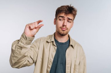 Genç bir adam hafif bir ifadeyle içeride duruyor, parmaklarını kullanarak küçük bir miktar gösteriyor. Rahat giyimi ve şakacı vücut dili dostça atmosfere katkı sağlıyor..