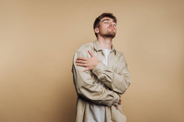 A young man stands confidently against a neutral background, crossing his arms and displaying a relaxed yet assertive pose. His outfit reflects modern fashion trends.
