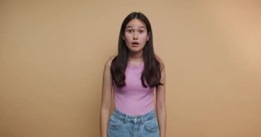 Genç kadın görüntülerinde şok ve şaşkınlık, geniş gözler ve açık bir ağızla bej arka planda sanatsal bir portrede vurgulanmış.