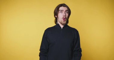 Genç adamın bej arka planda ellerini göğsünün yakınına koyarken sevinç ve heyecanı ifade eden görüntüleri.