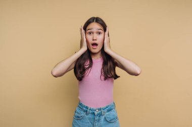 Elleri bej arka planda olan şaşırmış genç bir kadın..