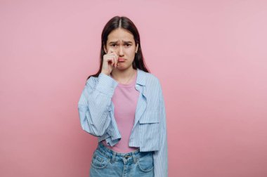 Üzgün bir ifadesi olan genç bir kadın pembe bir arka planda gözyaşı siliyor..