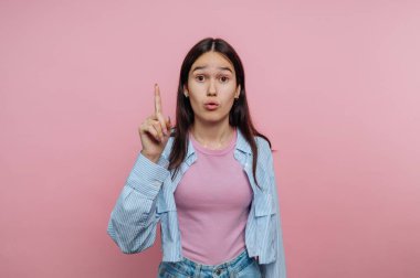 Pembe arka planı işaret eden şaşırmış bir yüzü olan genç kadın..