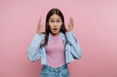 Elleri pembe arka planda olan şaşırmış genç bir kadın..