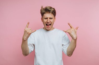 Beyaz tişörtlü genç adam pembe arka planda taş el hareketleri yapıyor..