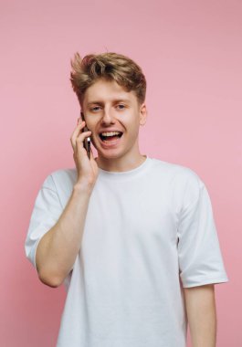 Pembe arka planda telefonla konuşan genç adam.