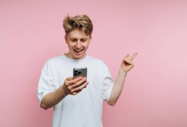 Genç adam pembe arka planda akıllı telefona heyecanla bakıyor..