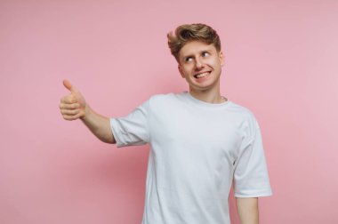 Beyaz tişörtlü genç adam pembe arka planı onaylıyor..