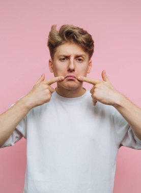 Hüzünlü bir ifadeyle pembe arka planda kaşlarını gösteren genç bir adam..