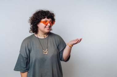 Kıvırcık saçlı, turuncu güneş gözlüğü takan ve günlük kıyafetler giyen bir kadın.