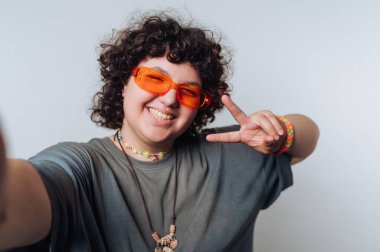 Kıvırcık saçlı, turuncu güneş gözlüğü takan ve barış işareti yapan biri..