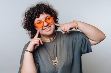 Kıvırcık saçlı, turuncu güneş gözlüğü takan ve gülümseyen biri..