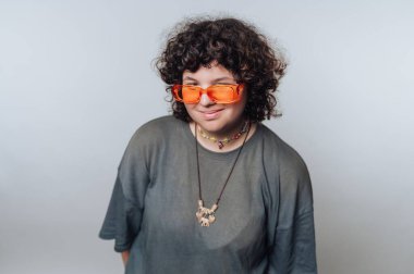 Turuncu güneş gözlüğü takan, günlük kıyafetler giyen, gülümseyen biri..