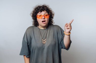 Kıvırcık saçlı, turuncu güneş gözlüklü ve gri gömlekli, yukarı doğru bakan biri..