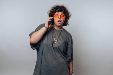 Kıvırcık saçlı, turuncu güneş gözlüğü takan ve gri tişörtlü, telefonla konuşan biri..