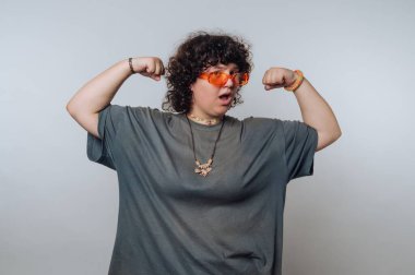 Kıvırcık saçlı ve kaslarını kasan turuncu güneş gözlüklü biri..