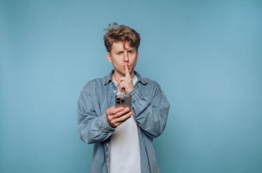 Akıllı telefon tutan genç adam, susma hareketi yapıyor..