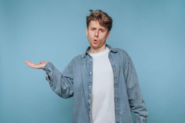 Kot gömlekli genç adam mavi arka planda el kol hareketi yapıyor..