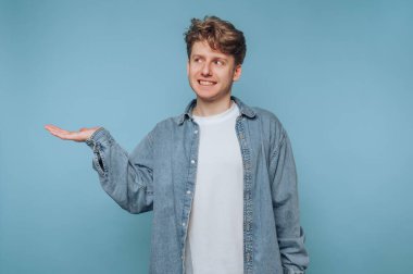 Kot gömlekli genç adam mavi arka planda el kol hareketi yapıyor..