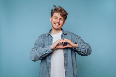 Genç adam mavi arka planda elleri olan bir kalp yapıyor..