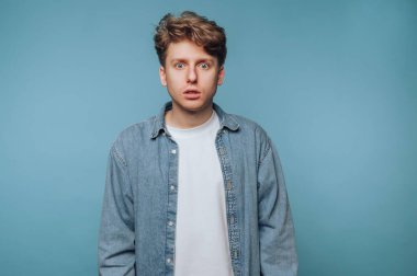 Kot gömlekli genç adam mavi arka plana şaşırmış görünüyor..