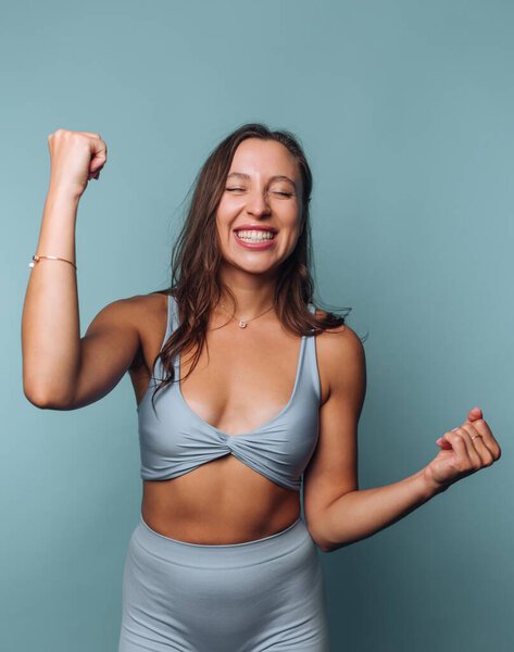 Smiling woman in athletic wear celebrating with clenched fists.