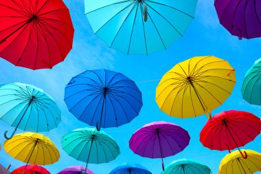 Gökyüzünde parlak renkli şemsiyeler var. Sokakta güneş ve yağmur koruması.