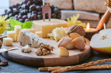 Farklı peynirlerden peynir tabağı - Emmental, ev yapımı, parmesan peyniri, mavi peynir, ekmek çubuğu, ceviz, kuru üzüm, armut, siyah masada üzüm